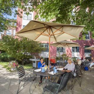 People sitting at an outdoor patio under large umbrellas near a building.