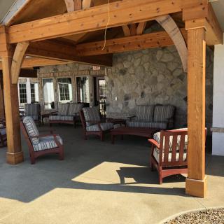 A cozy outdoor patio area with wooden beams, featuring cushioned armchairs and a couch against a stone wall.
