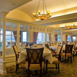 An elegant dining room with neatly arranged tables and chairs, illuminated by chandeliers.
