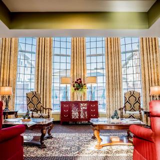 A spacious and elegantly decorated living room with large windows, patterned curtains, and stylish furniture.