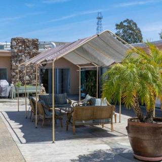 A sunny patio with comfortable outdoor seating under a canopy, surrounded by lush plants.