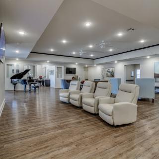A modern open living space featuring comfortable recliners, a piano, and sleek wood flooring.