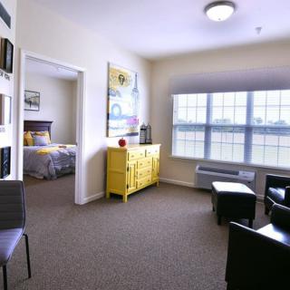 A modern apartment living room with a bright yellow accent piece and natural light streaming in through large windows.