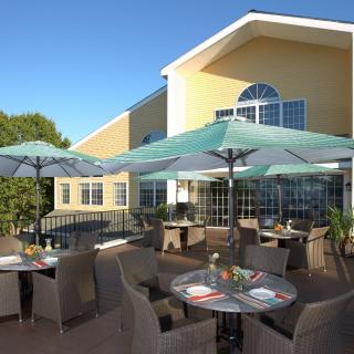An outdoor dining area with tables, chairs, and umbrellas on a patio beside a building.
