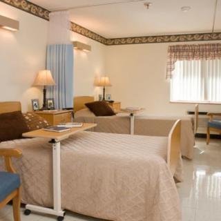 A clean and well-organized hospital room with two patient beds and bedside tables.