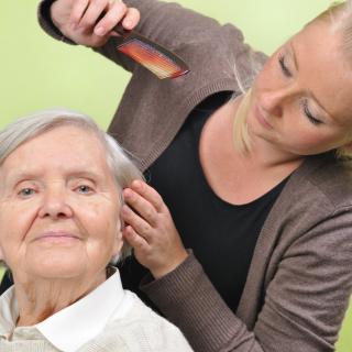A caregiver gently combs the hair of a senior woman.