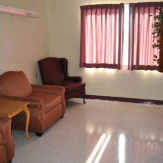 A simple living room with a sofa, armchair, and table near a window with curtains.