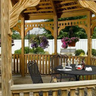 A cozy wooden gazebo featuring a dining table and chairs, surrounded by hanging plants in a garden setting.