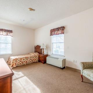 A cozy bedroom with a single bed, two windows, a chair, and a dresser.