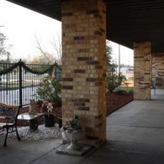 An outdoor patio with brick pillars, seating, and decorative plants alongside a fenced area.