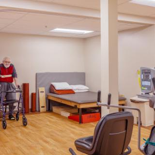 A spacious rehabilitation room equipped for elderly care, featuring a bed and supportive medical equipment.