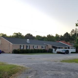 A view of a brick residential building with a parking lot surrounded by greenery.