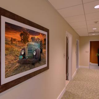 A hallway with a framed painting of an old tractor at sunset on the wall.