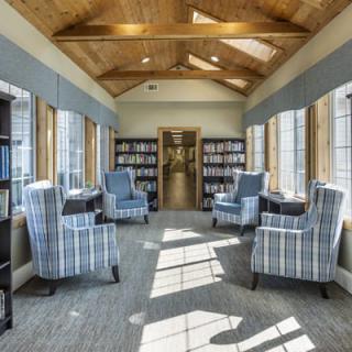 A cozy library seating area with comfortable chairs and ample natural light streaming through large windows.