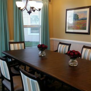 A well-decorated dining room featuring a long wooden table with striped chairs, accented by a chandelier and vases of red flowers.