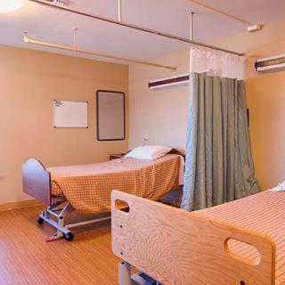 An empty hospital room with two beds and a privacy curtain.
