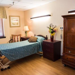 A cozy hospital room with a single bed, wooden furniture, and a vase of flowers.