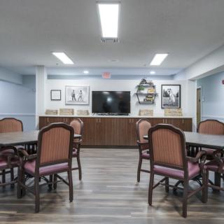 A spacious meeting room with tables and chairs, featuring artwork on the walls and a large television.