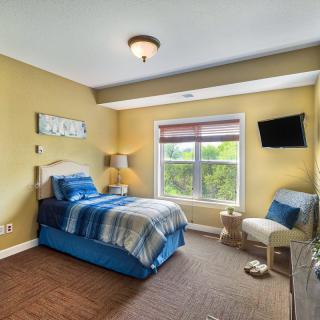 A cozy bedroom with a single bed, window view, and a wall-mounted television.