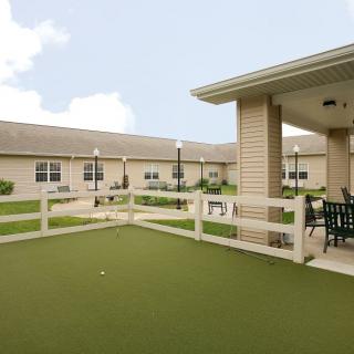 A view of a courtyard with a well-maintained lawn, surrounded by a building and featuring outdoor seating.