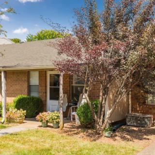 A brick house with a front yard featuring shrubs and trees on a sunny day.