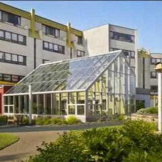 A modern building with an attached glass greenhouse surrounded by greenery.