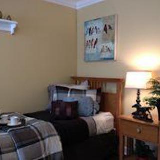 A cozy bedroom with a neatly made single bed, a nightstand with a lamp, and stylish wall art.