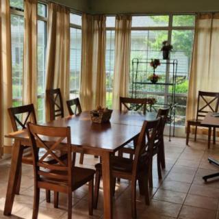 A cozy dining room with wooden furniture and large windows letting in natural light.