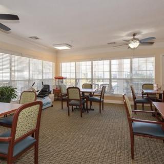 A cozy dining area with multiple tables and chairs, surrounded by large windows and equipped with ceiling fans.