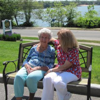 Two individuals sitting on a bench by the lake, enjoying a sunny day.