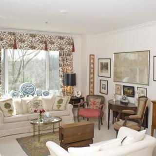 A cozy living room with elegant furnishings and decor, featuring a large window and various artworks on the walls.