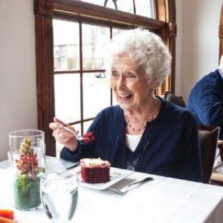 An elderly woman is enjoying a piece of cake at a restaurant.