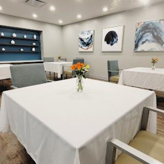 A neatly arranged dining area featuring white tablecloths, floral centerpieces, and contemporary artwork.