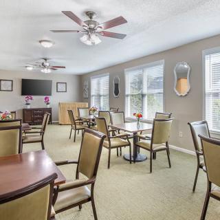 A bright dining room with several tables and chairs, ceiling fans, and large windows.