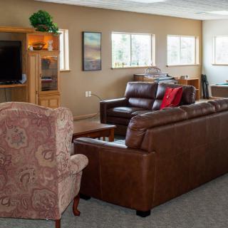 A cozy living room with comfortable leather sofas, a patterned armchair, and a wooden cabinet housing a television.