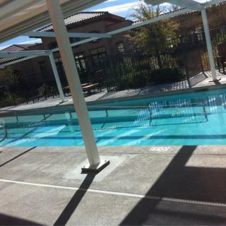 An outdoor swimming pool with surrounding buildings and clear blue water under a sunny sky.