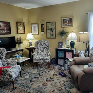 A cozy living room with various artworks on the walls, two patterned chairs, a sofa, and a television.