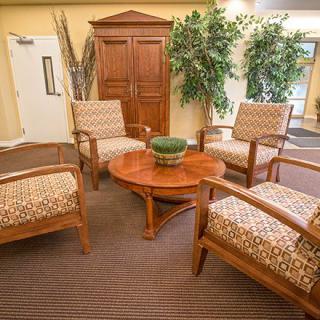 A cozy waiting area with four upholstered chairs around a wooden coffee table, complemented by greenery and a cabinet in the background.