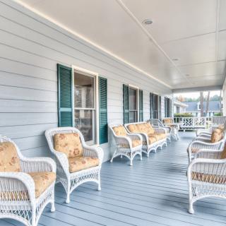 A view of a spacious porch with wicker chairs and cushions, offering a comfortable outdoor seating area.