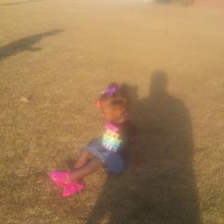 A young child sitting on the grass, enjoying a sunny day outdoors.