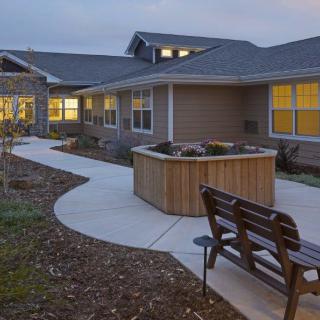 A well-lit residential building with a pathway and a bench in the foreground during the evening.