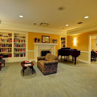 A cozy living room with a fireplace, a grand piano, and a bookshelf filled with books.