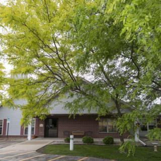 A small building surrounded by lush green trees and a parking area.