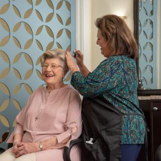 An elderly woman is getting her hair styled by a hairdresser in a salon.