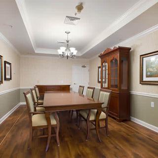 A spacious dining room with a long wooden table and matching chairs, featuring elegant ceiling lights and decorative paintings on the walls.