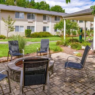 A cozy outdoor patio area with a fire pit and several chairs, surrounded by well-maintained landscaping at an apartment complex.