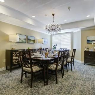 A well-decorated dining room featuring a large table with chairs, elegant chandelier, and framed artwork on the walls.