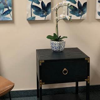 A small black table with a potted orchid, accompanied by abstract blue artwork on the wall.
