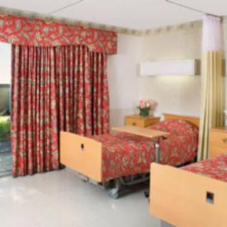 A hospital room with two beds and floral curtains.