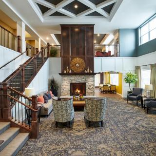A modern lobby area featuring a central fireplace, comfortable seating, and a staircase leading to an upper floor.